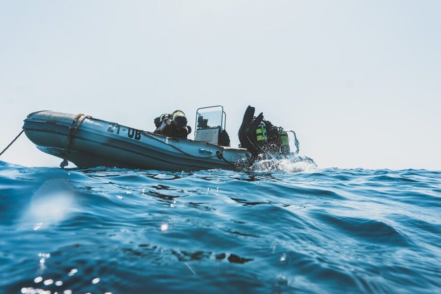 Scuba divers preparing gear on an inflatable dive boat under a clear sky