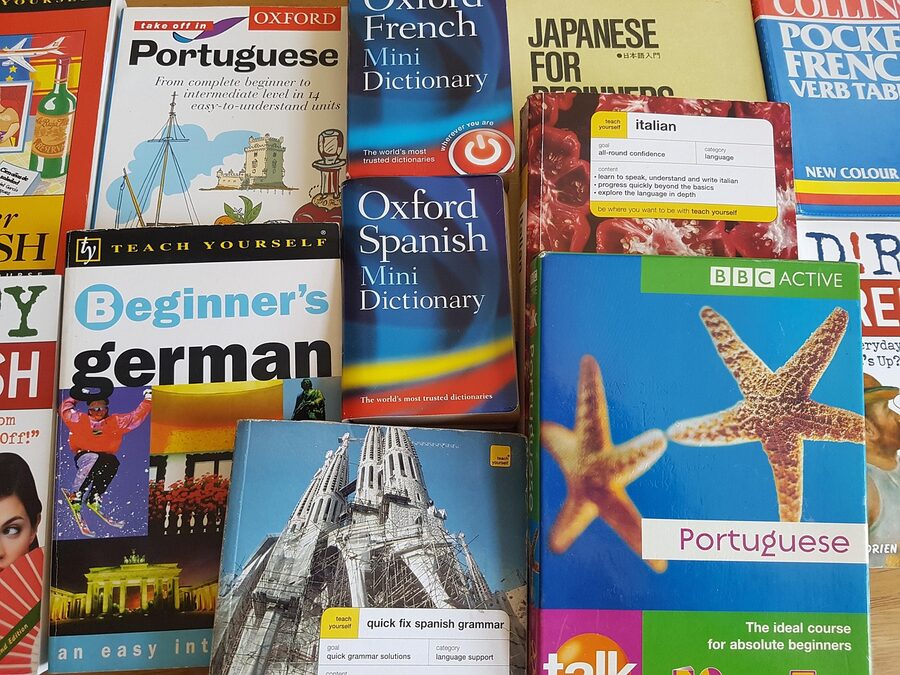 A stack of language learning books and phrasebooks open on a desk