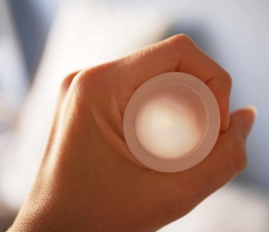 Silicone menstrual cup held in a palm against a neutral background