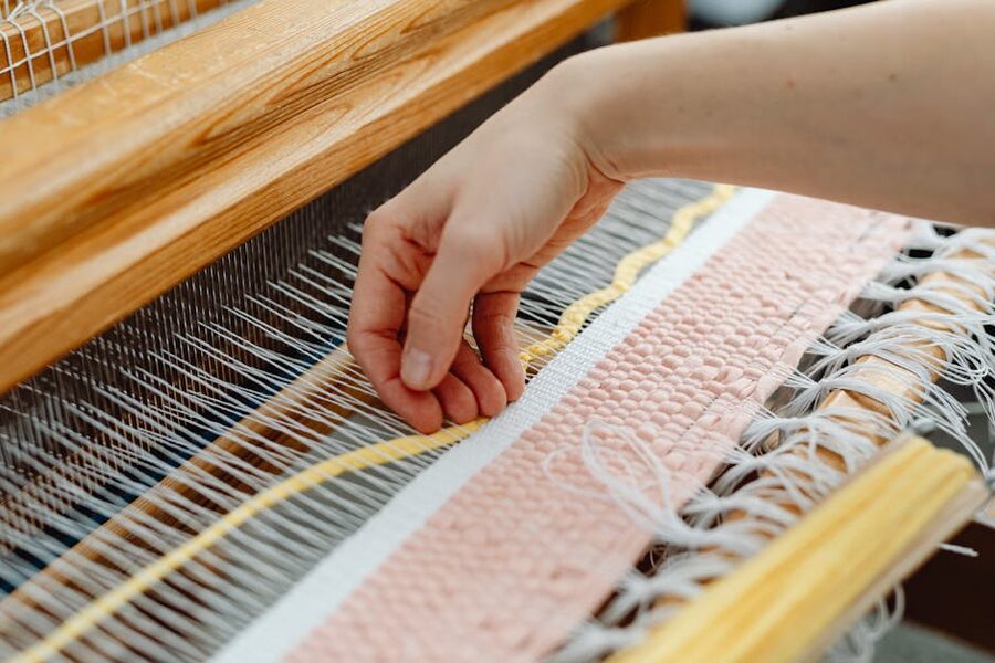 Hands weaving brightly coloured threads on a traditional wooden loom