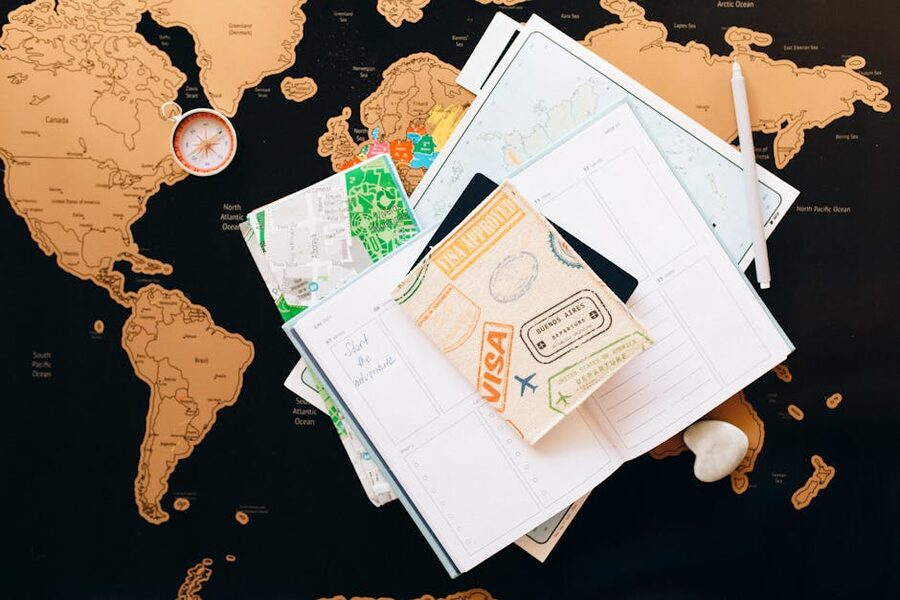 Travel planning items spread out on a world map, including a notebook, compass, and a small bag
